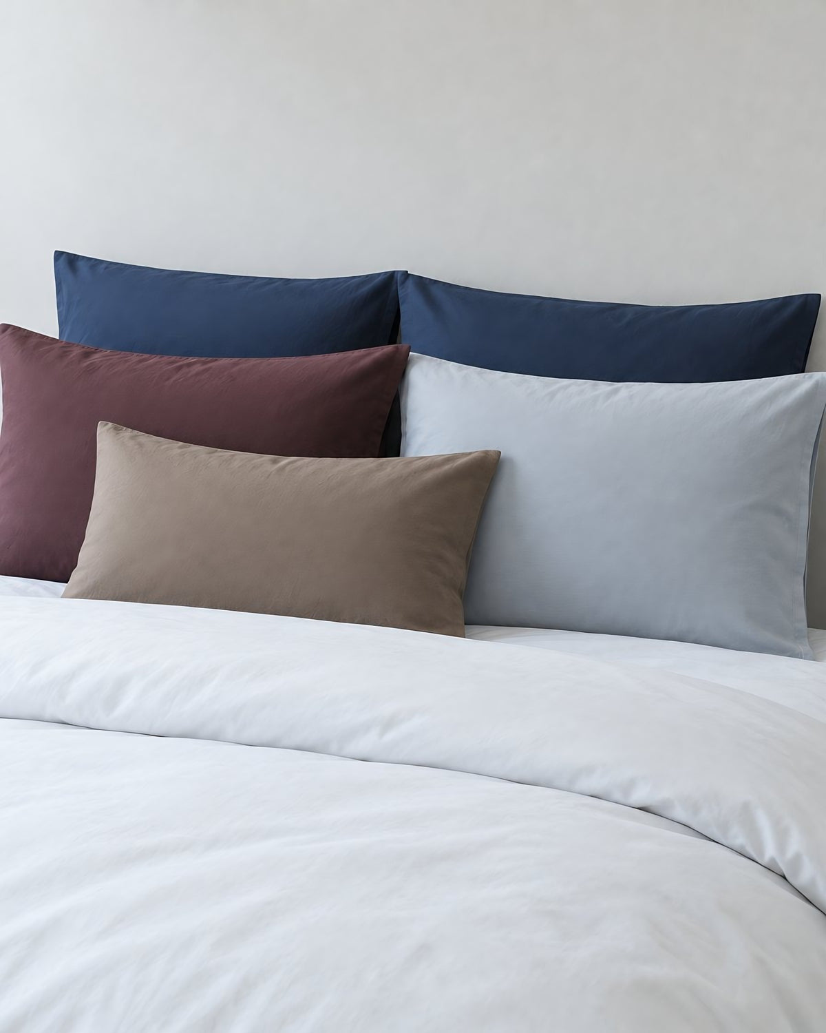 Navy, burgundy, taupe and grey plain cotton pillowcases seen from above with a breakfast tray of coffee and croissants