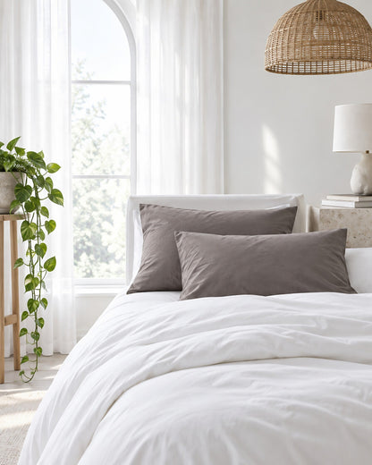 Taupe plain cotton pillowcases beneath an arched window with a trailing pothos and rattan pendant