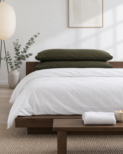 Olive green plain cotton pillowcases in a calm Japandi bedroom on a low dark-oak bed