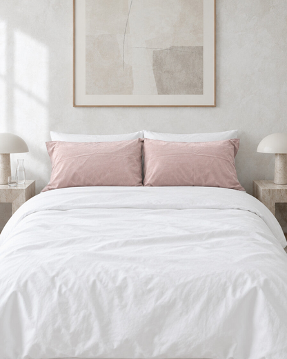 Pale pink plain cotton pillowcases on a white made bed against a limewashed plaster wall