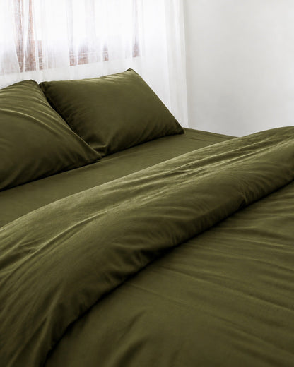 Two pillows in Juniper Green silky cotton pillowcases at the head of a made bed by a sheer curtain