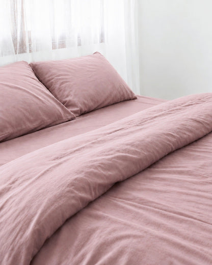 Two pillows in Rose Pink silky cotton pillowcases at the head of a made bed by a sheer curtain