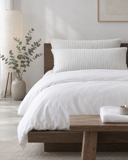 Blue Pinstripe cloud cotton pillowcases on long pillows at a dark-oak platform bed, a paper lantern and eucalyptus beside.