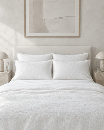 White cloud cotton pillowcases against a limewashed plaster wall between travertine bedside tables