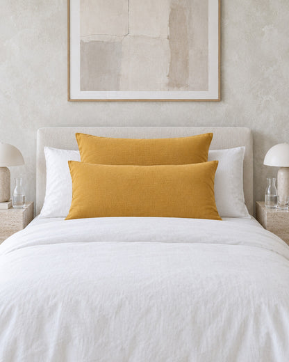 Mustard cloud cotton pillowcases against a limewashed plaster wall between travertine bedside tables