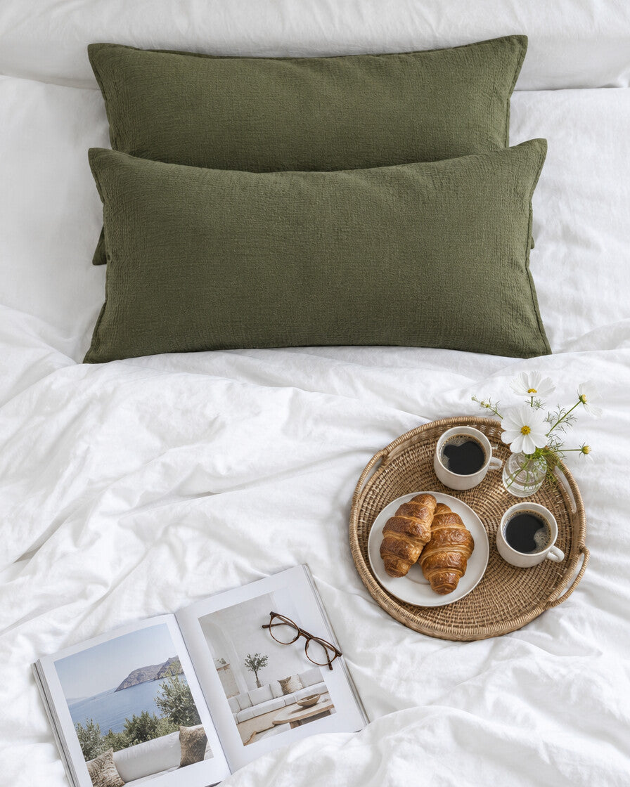 Juniper green cloud cotton pillowcases seen from above with a breakfast tray of coffee and croissants