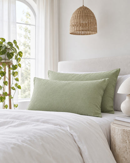 Mint green cloud cotton pillowcases beneath an arched window with a trailing pothos and rattan pendant