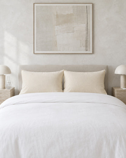 Cream cloud cotton pillowcases against a limewashed plaster wall between travertine bedside tables