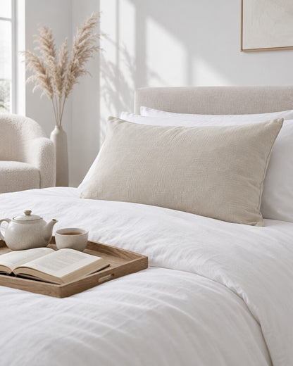 Oat milk cloud cotton pillowcases with a tea tray and open book, a boucle armchair in the corner