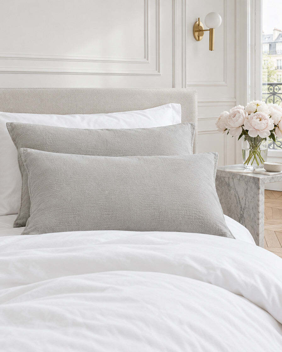 Warm grey cloud cotton pillowcases in a Parisian bedroom with panelled walls and fresh peonies