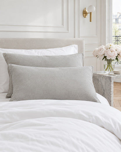 Warm grey cloud cotton pillowcases in a Parisian bedroom with panelled walls and fresh peonies