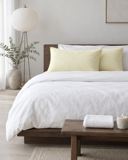 Soft pale yellow cloud cotton pillowcases in a calm Japandi bedroom on a low dark-oak bed