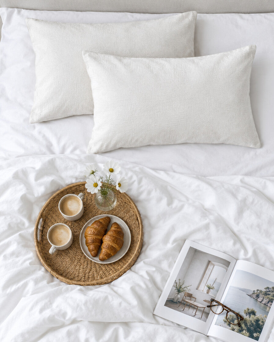 Off white cloud cotton pillowcases seen from above with a breakfast tray of coffee and croissants