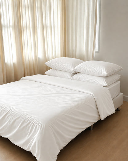 Milky White Silky Cotton sateen pillowcases on a made white bed by sheer curtains