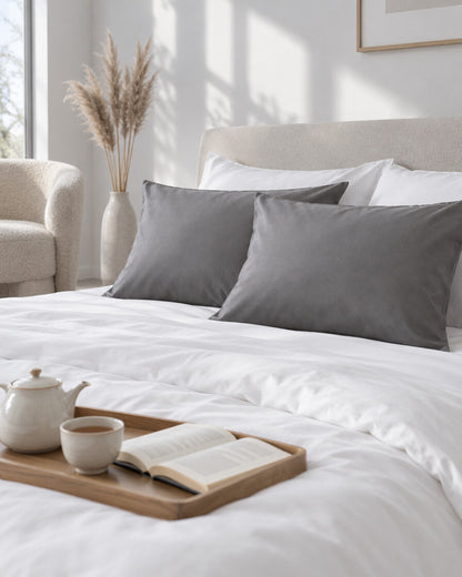 Single grey silky cotton pillowcases with a tea tray and open book, a boucle armchair in the corner
