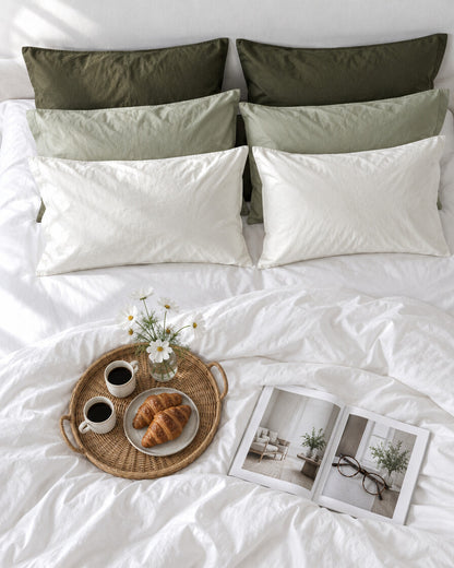 Olive green and cream silky cotton pillowcases seen from above with a breakfast tray of coffee and croissants