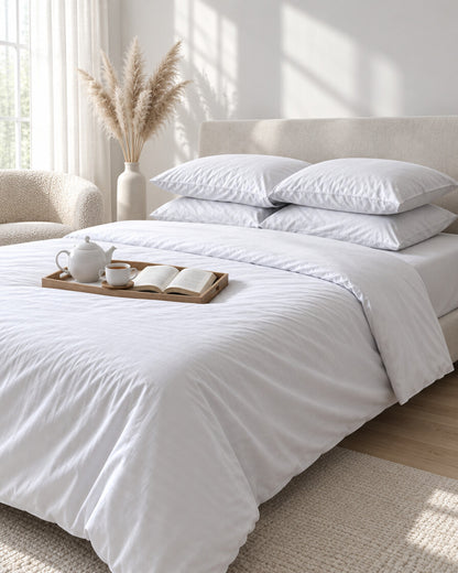 White silky cotton pillowcases with a tea tray and open book, a boucle armchair in the corner