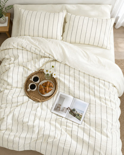 Cream pinstripe cloud cotton bedding set seen from above with a breakfast tray of coffee and croissants