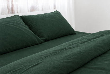 Two pillows in Forest Green plain cotton pillowcases at the head of a made bed with a matching bottle-green sheet and duvet cover