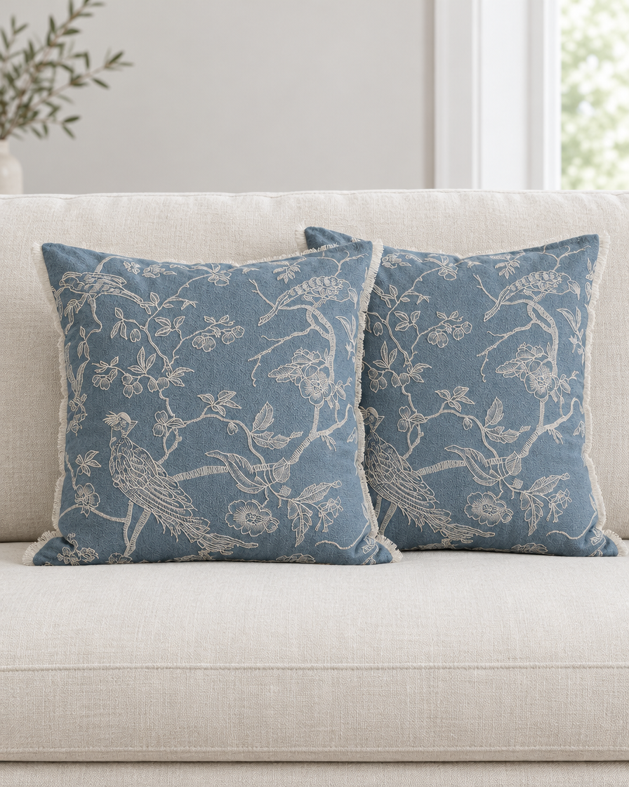 Two dusty blue Bird Embroidery cushion covers on a cream linen sofa