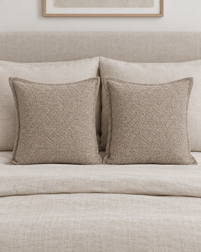 Two Taupe Heathered Jacquard cushion covers on a made bed with oatmeal linen bedding