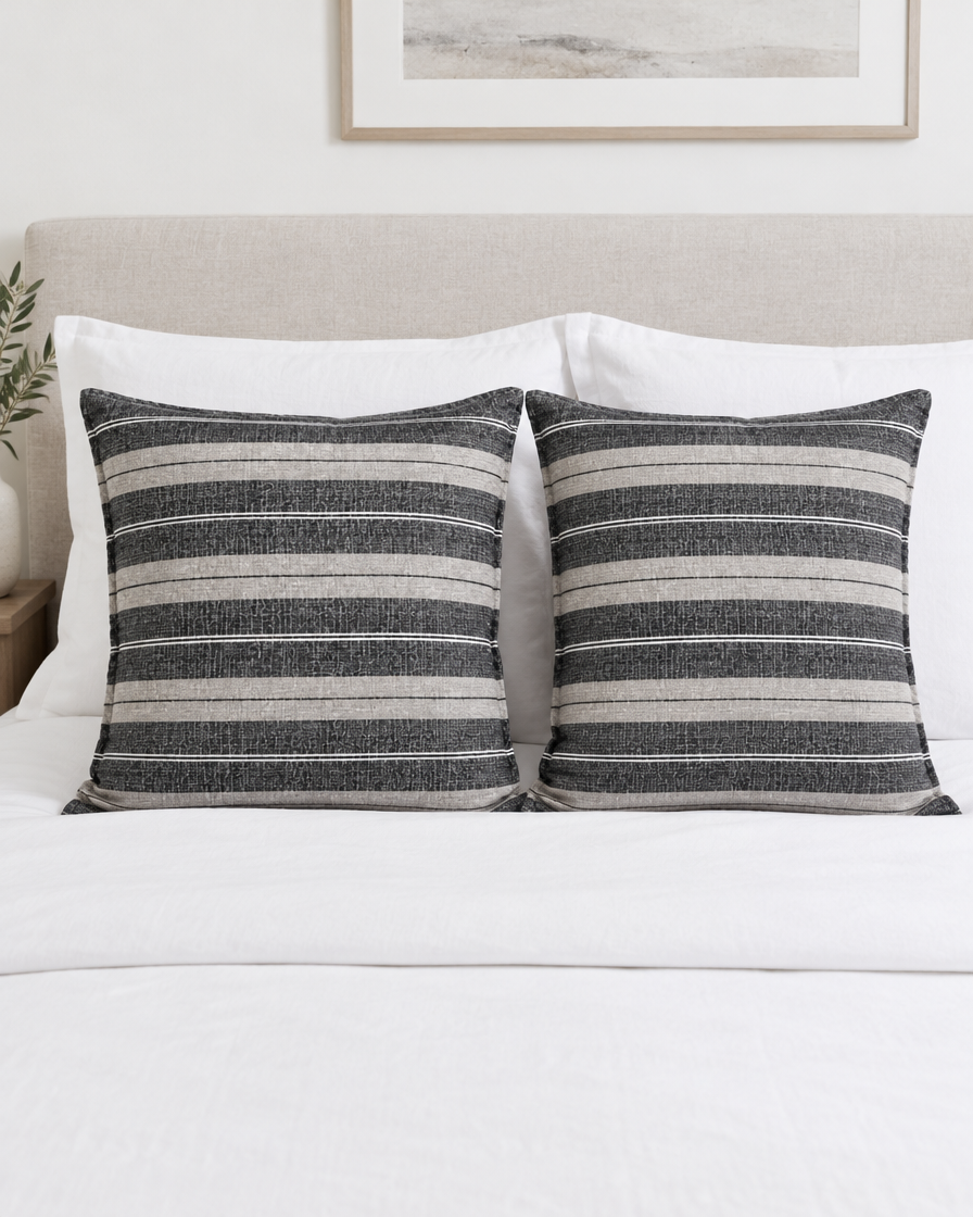 Two Charcoal Wide Stripe Jacquard Linen cushion covers on a made bed with white bedding
