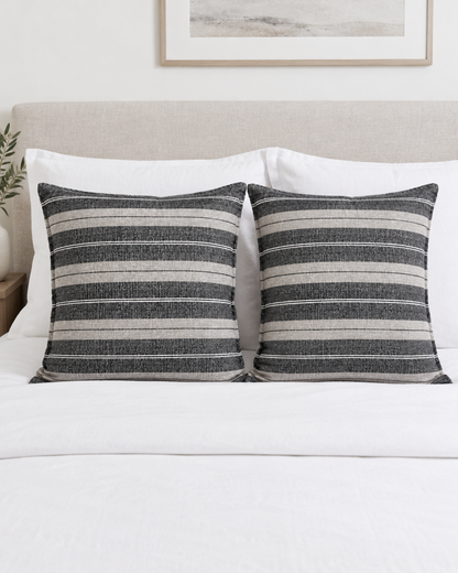 Two Charcoal Wide Stripe Jacquard Linen cushion covers on a made bed with white bedding