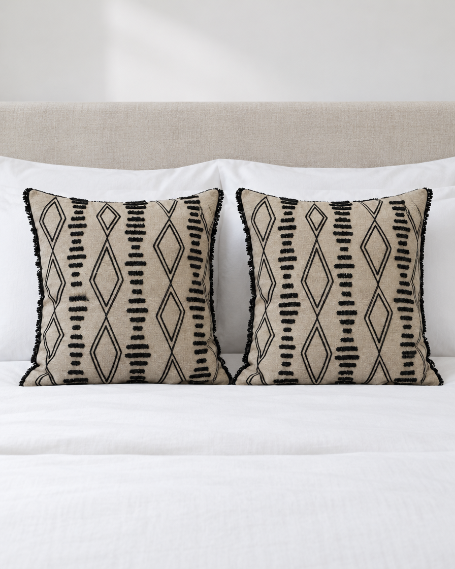Two Sand & Black Ikat Embroidery cushion covers on a made bed with white bedding