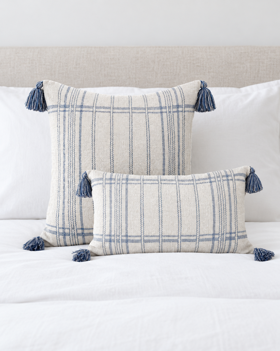 Ivory and blue striped square and check lumbar cushion covers with blue tassels on a made bed