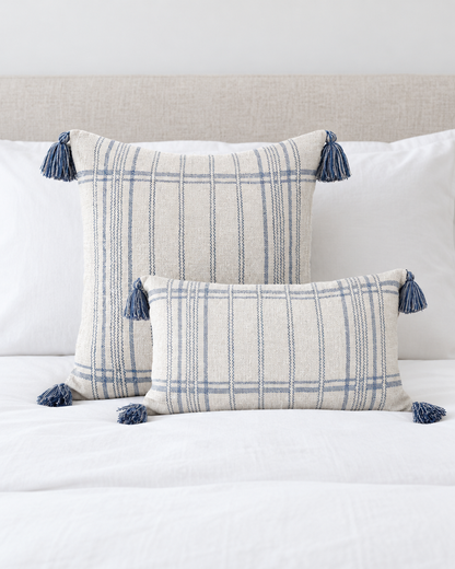 Ivory and blue striped square and check lumbar cushion covers with blue tassels on a made bed