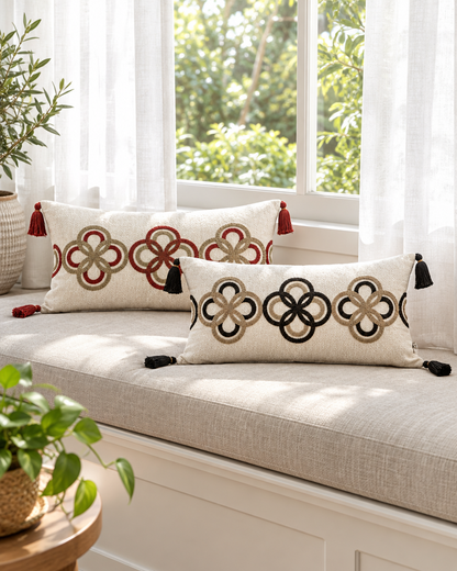 Ivory lumbar cushions with red and black ring embroidery and corner tassels on a sunlit window seat