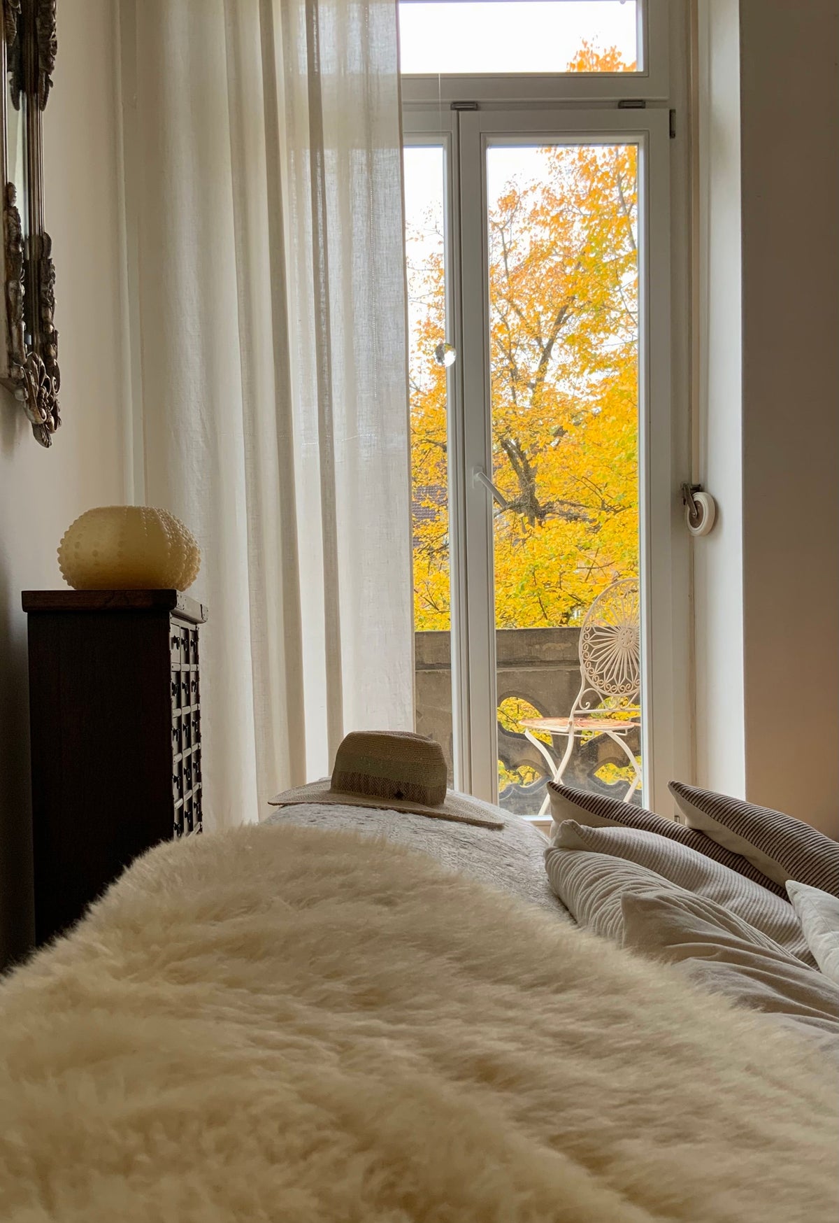 A bed beside a tall window with autumn trees outside