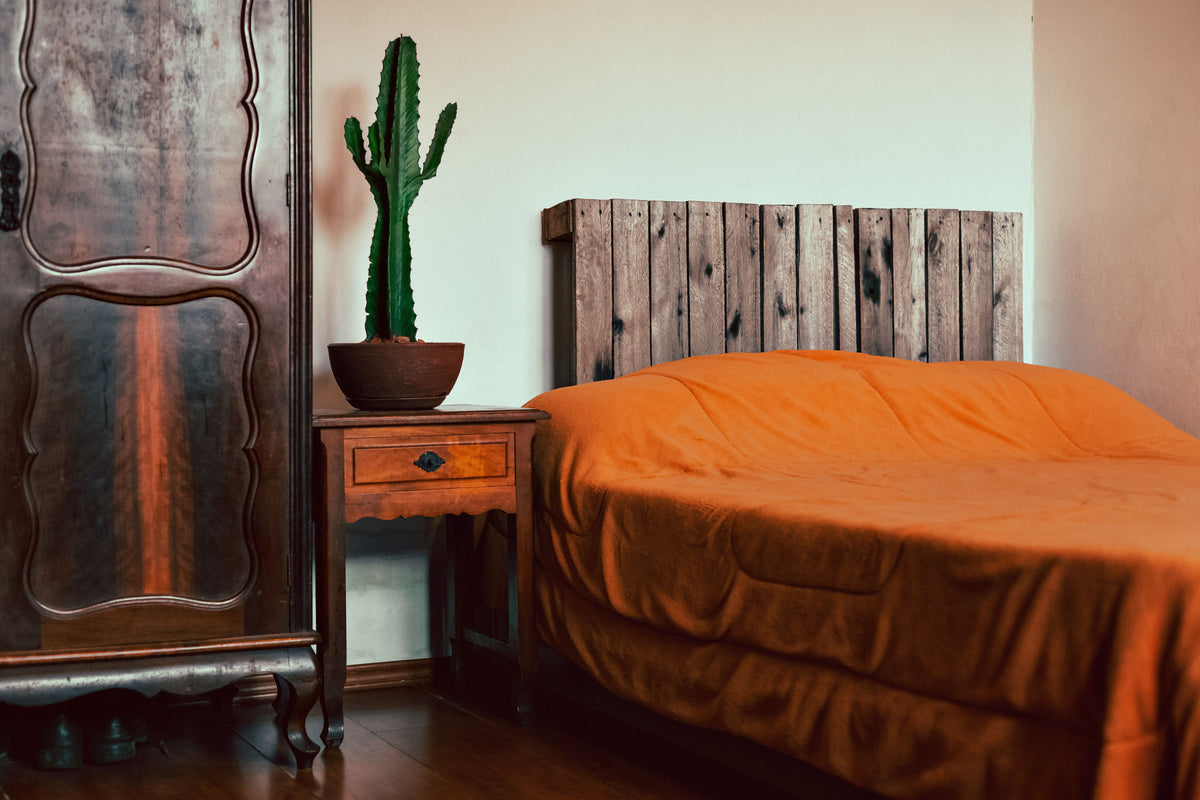 A bed in burnt orange bedding beside an antique wardrobe