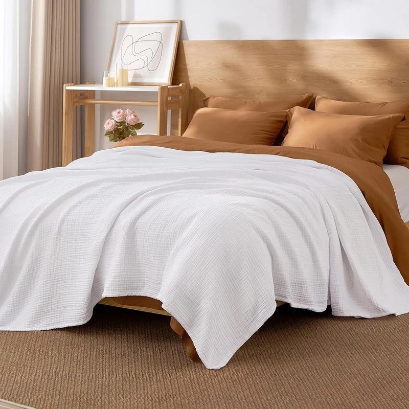 Off white cloud cotton throw blanket folded across a made bed with tan bedding