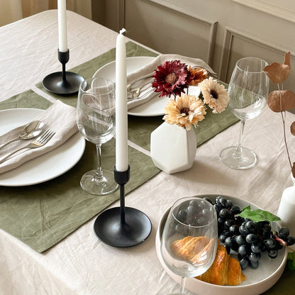 Natural linen tablecloth on a laid table with a moss green runner, candles and autumn flowers