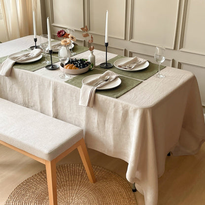 Natural linen tablecloth hanging over the edge of a dining table set for four with a green runner