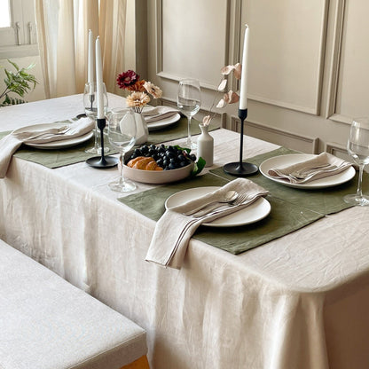 Linen tablecloth on a set dining table with candles, grapes and striped napkins