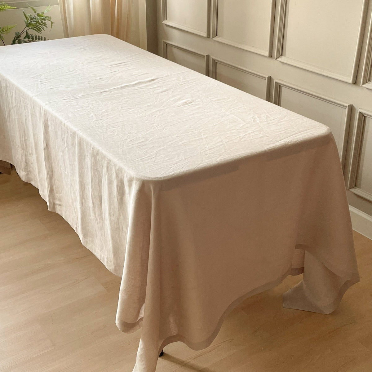 Natural linen tablecloth draped over a bare rectangular dining table, showing the fall of the flax