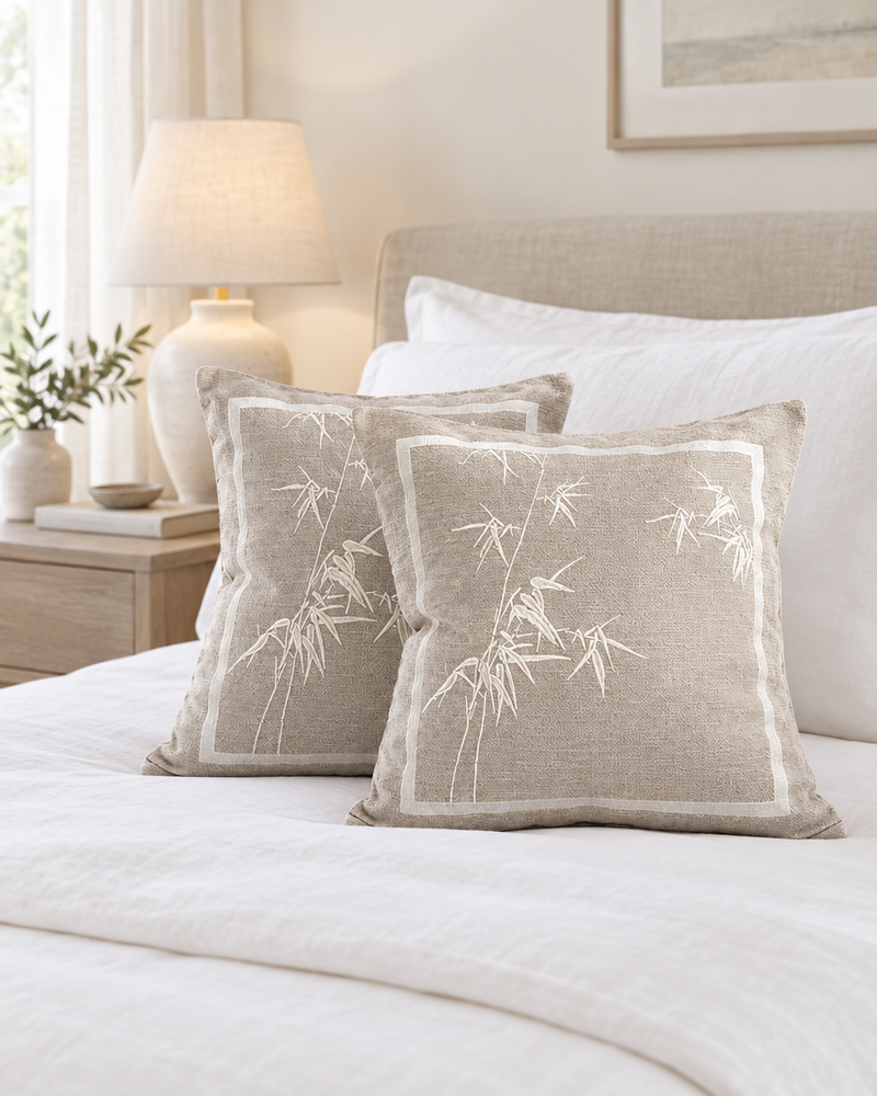 Taupe cushions with ivory bamboo embroidery and border on a made bed with white linen