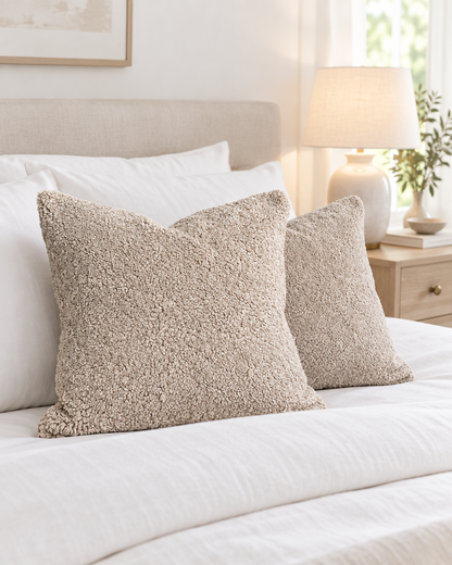 Beige teddy faux fur cushions on a made bed with crisp white linen and a ceramic bedside lamp