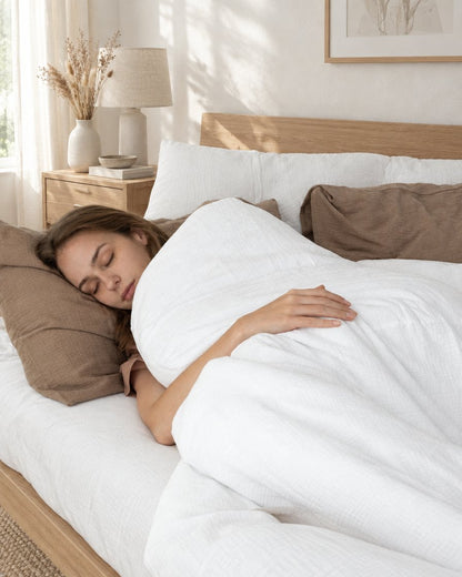 Woman asleep on white and mocha two-tone cloud cotton bedding, in a calm sunlit Scandinavian bedroom