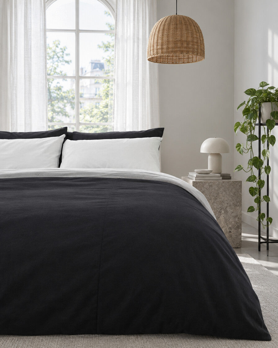 Charcoal and white two-tone plain cotton bedding beneath an arched window with a trailing pothos and rattan pendant
