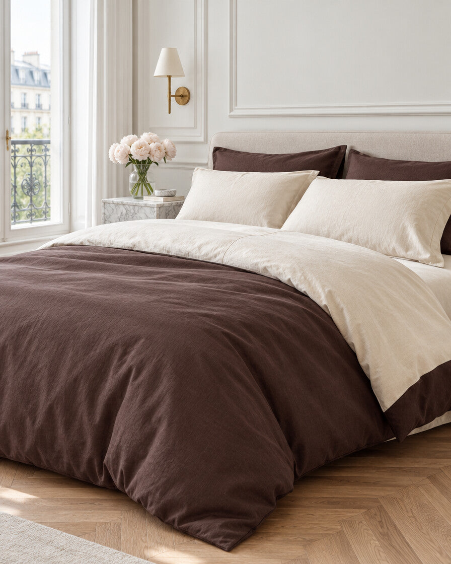 Chocolate brown and cream two-tone plain cotton bedding in a Parisian bedroom with panelled walls and fresh peonies