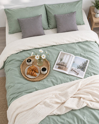 Sage green and cream two-tone plain cotton bedding seen from above with a breakfast tray of coffee and croissants