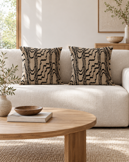 Square sand cushions with black wood grain embroidery on a cream sofa beside an oak coffee table